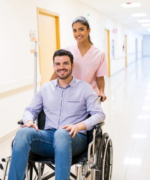 Smiling orderly pushing discharged mid adult patient on wheelchair at corridor in hospital